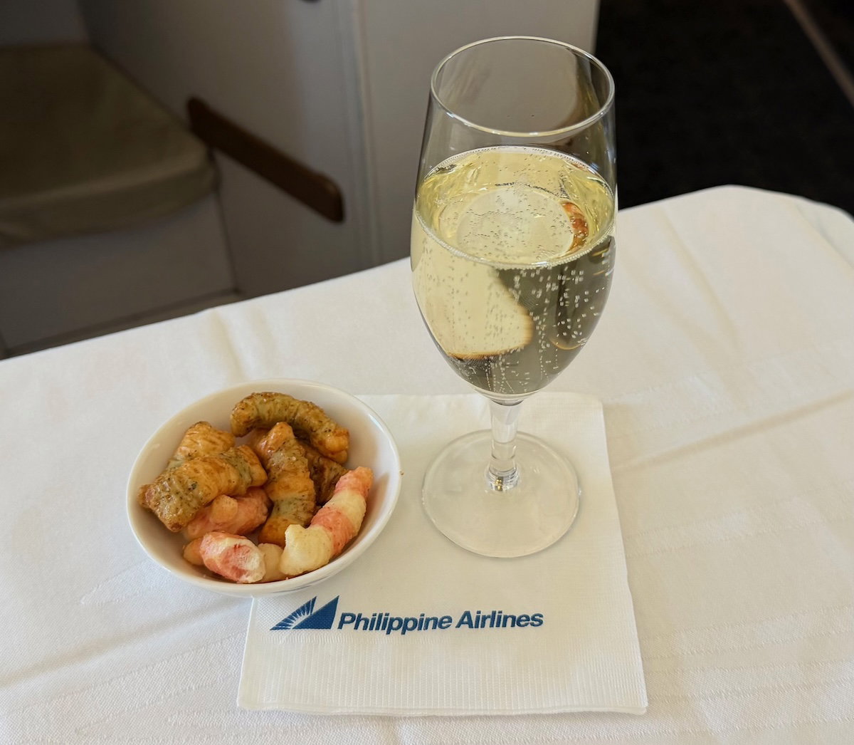 Glass of sparkling wine served with a small dish of seaweed and prawn crackers on a business class tray table