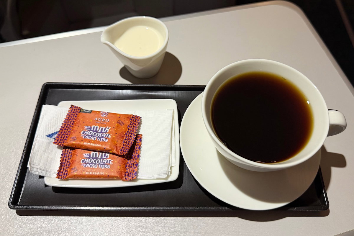 Cup of coffee on a tray with a small milk pitcher and chocolates in Philippine Airlines business class